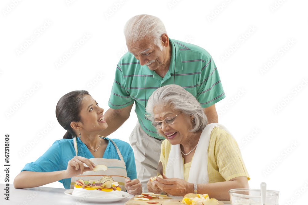 Grandmother and granddaughter working in the kitchen while grandfather looks on Grandmother and granddaughter working in the kitchen while grandfather looks on