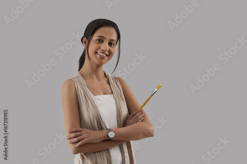 Portrait of young woman holding paintbrush isolated over gray background 