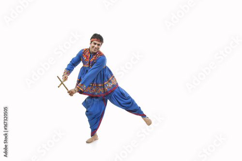Portrait of happy young man in traditional wear performing Dandiya Rass over white background