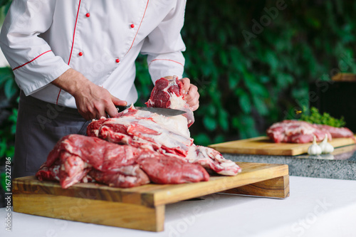 A man cook cuts meat with a knife in a restaurant.