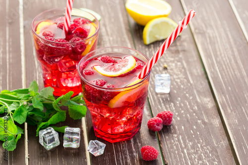 Summer drink with raspberries, lime and ice on a old wooden table