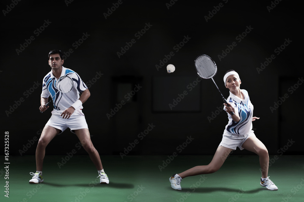 Man and woman playing badminton doubles at court Man and woman playing badminton doubles at court