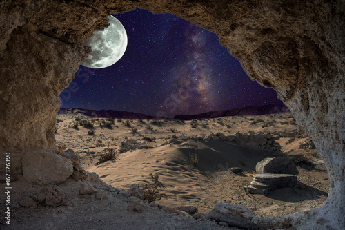 Obraz Nierealny nocny krajobraz przez jaskinię z mleczną, zaćmieniem księżyca i pustynią z ruinami starożytnych kolumn.