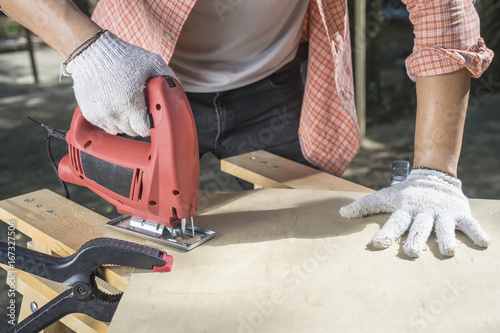Wood worker cutting wooden panel with jig saw.