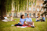 Couples of multi ethnic students are preparing for test, sitting in the park, chatting, smile, enjoying, helping each other with studies. All dressed in comfortsble casual wear