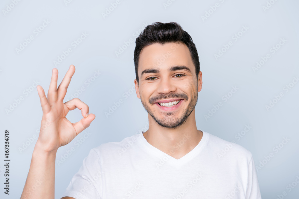 Young cheerful successful guy on the pure light blue background is smiling, wearing casual outfit and is showing ok sign Young cheerful successful guy on the pure light blue background is smiling, wearing casual outfit and is showing ok sign