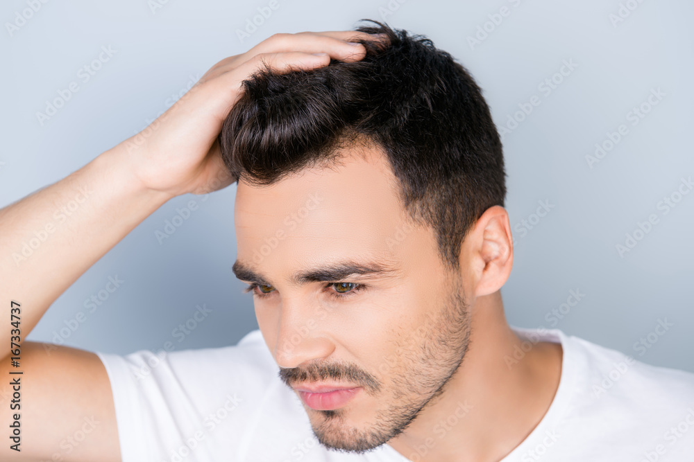High angle view of confident sexy handsome young brunet in white t shirt, standing on the pure background, fixing his perfect hairstyle. So hot and attractive, healthy and fashionable