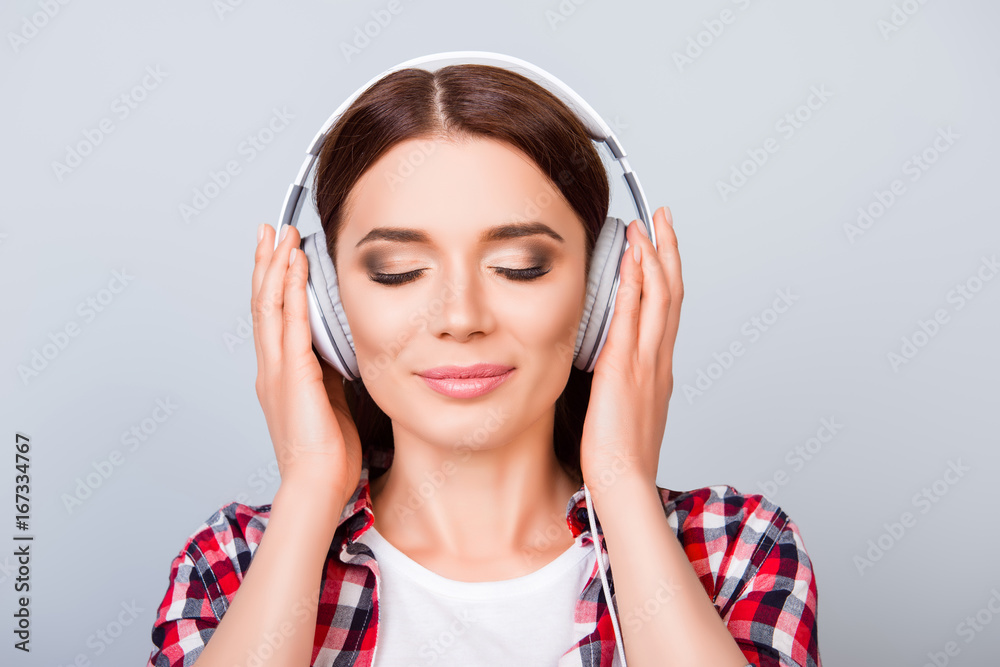 Charming young girl with closed eyes in modern headphones. She is dreamy and happy, listening to her favourite song, holding the earphones, on pure background Charming young girl with closed eyes in modern headphones. She is dreamy and happy, listening to her favourite song, holding the earphones, on pure background