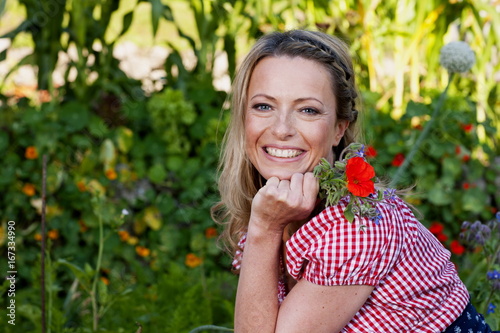 Glückliche Frau mittleren Alters im Garten mit einer roten Blume