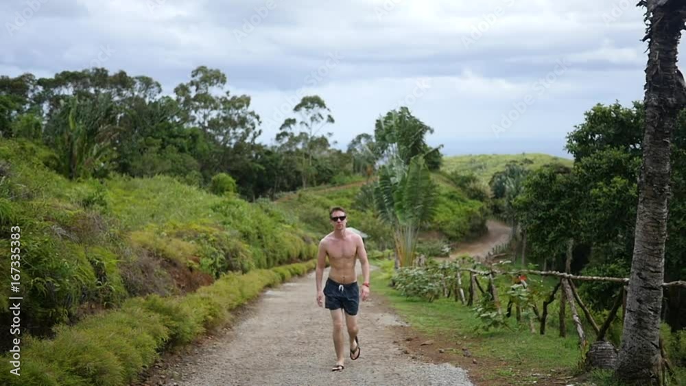 Slow motion, shirtless man walks in tropical landscape Slow motion, shirtless man walks in tropical landscape