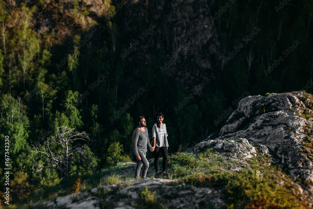 Obraz premium Loving couple at sunset standing on a cliff. A couple in love travels in the mountains. Couple travels. Lovers in nature. Man and woman watching the sunset. Lovers at sunset. Walk in the mountains