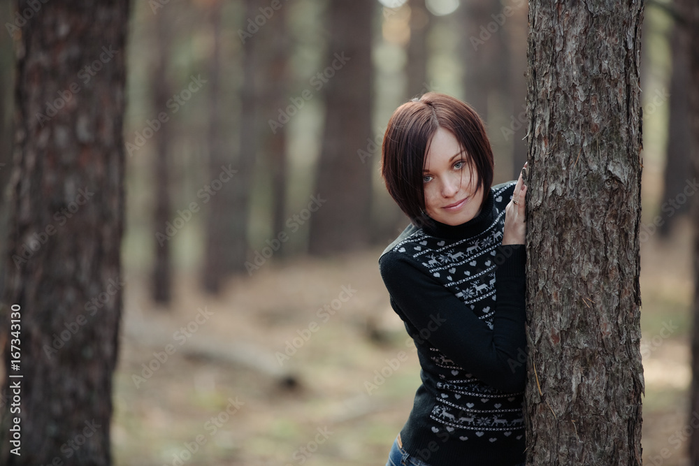 Beautiful young girl peeking from behind a pine trunk Beautiful young girl peeking from behind a pine trunk