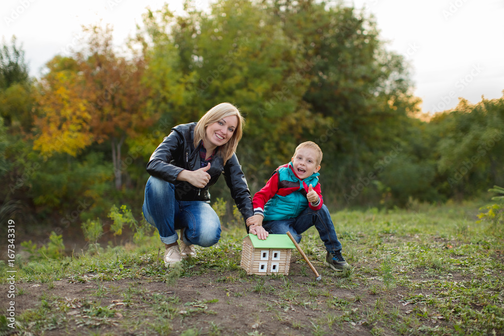 A small boy with his mother in the autumn forest gathered a wooden house designer, holding a hammer in his hand and very happy with his creation