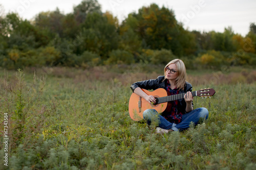  girl sits on the grass with a guitar playing, putting her hands on the strings