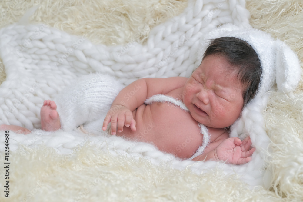 cute asian boy newborn portrait with white doll one month lie down and cry on white background fur . cute asian boy newborn portrait with white doll one month lie down and cry on white background fur .