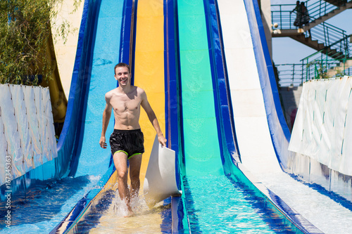 Young cheerful man has fun on vacation on a slide in the water park
