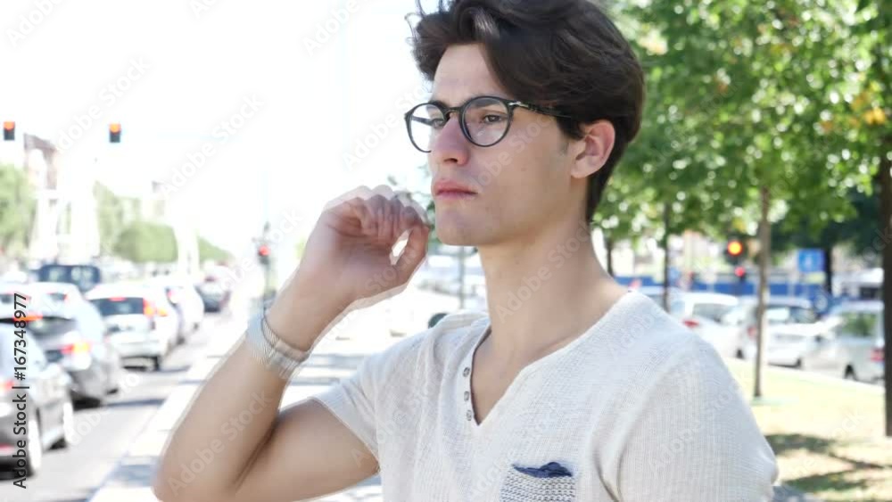 Young attractive man by city street waiting for someone, looking at cellphone while cars pass him by. Also looking at camera Young attractive man by city street waiting for someone, looking at cellphone while cars pass him by. Also looking at camera