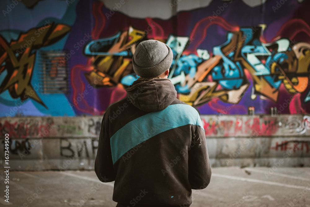 Graffiti artist standing near the wall - obrazy, fototapety, plakaty 