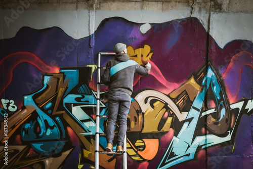 Graffiti artist standing on ladder and painting with aerosol spray on the wall
