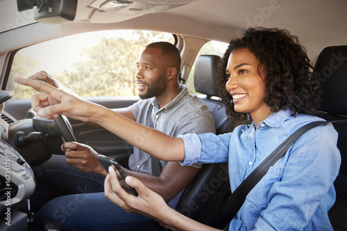 Foto Happy couple in car on a road trip navigate with smartphone