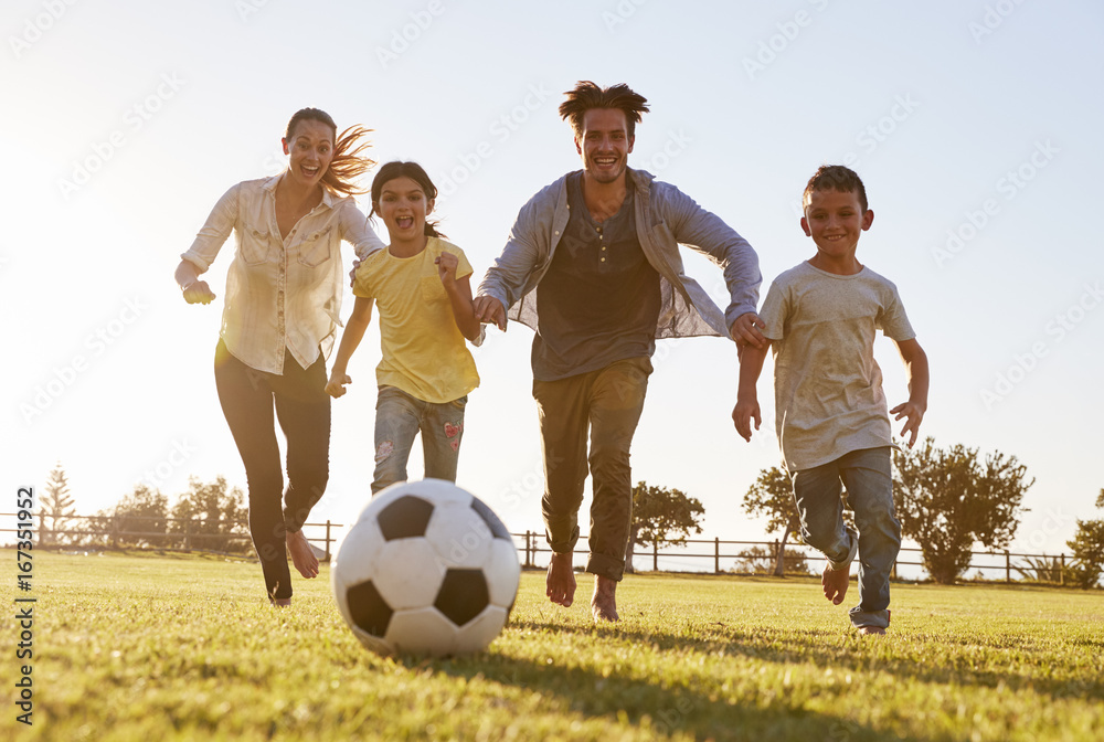 Obraz premium Young family chasing after a football in a park