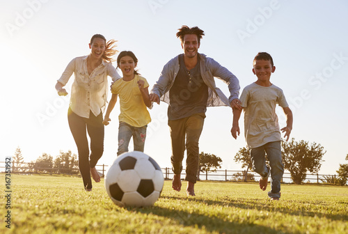 Young family chasing after a football in a park