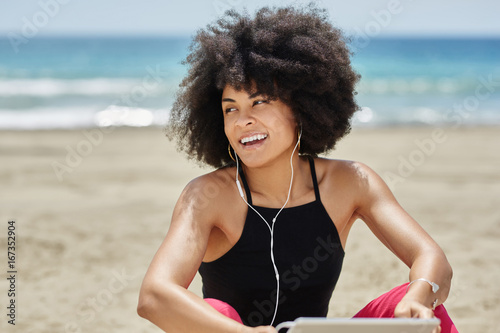 Happy afro american woman listening music on beach looking away