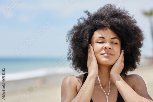 Afro american woman relaxing on beach listening music