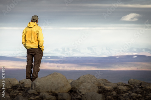 Man standing on mountain, looking relaxed towards snowy mountain range.