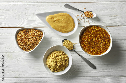 Mustard seeds, powder and sauces in dishes on wooden table