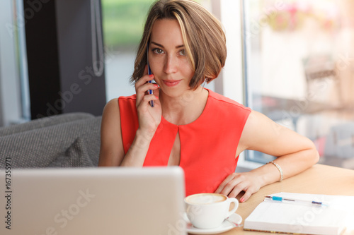 Cheerful business woman in the cafe talking by mobile phone