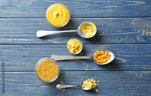 Mustard powder, seeds and sauces in dishes on wooden table