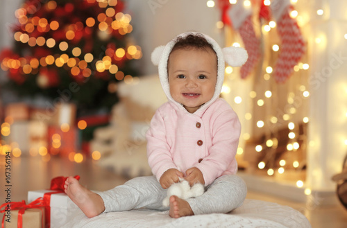 Cute little baby with toy sitting on floor in decorated for Christmas room
