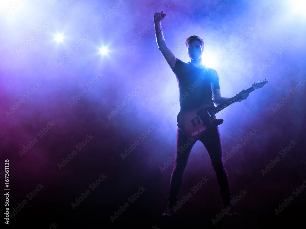 Silhouette of guitar player on stage on blue background with smoke and spotlights