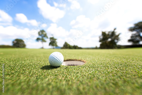 Golf ball near hole, background blue sky