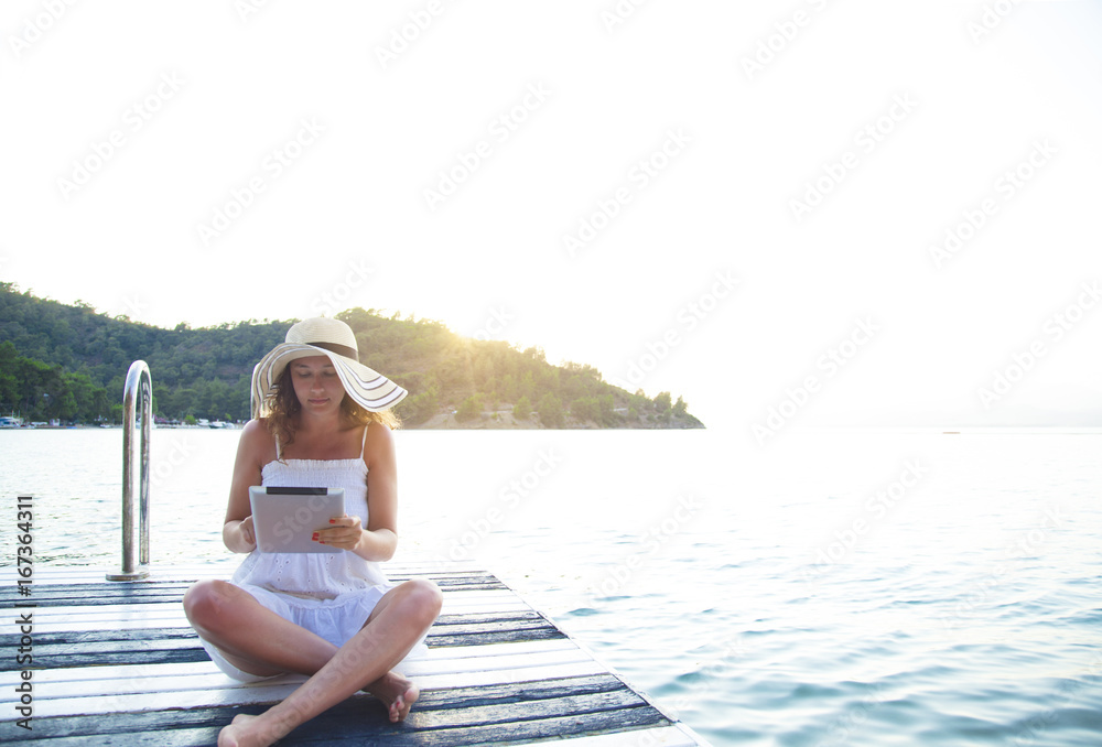 Young woman using digital tablet sitting on the pier