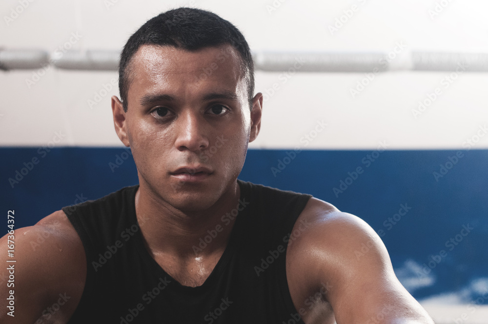 Portrait of sweaty latin american male boxer looking at camera confidently after working out in boxing gym Portrait of sweaty latin american male boxer looking at camera confidently after working out in boxing gym