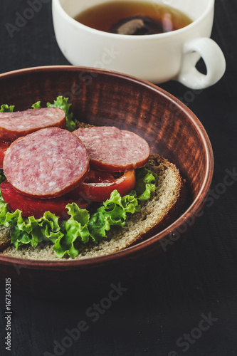 A sandwich: bread, a leaf of lettuce, paddy and sausage. Black background.
