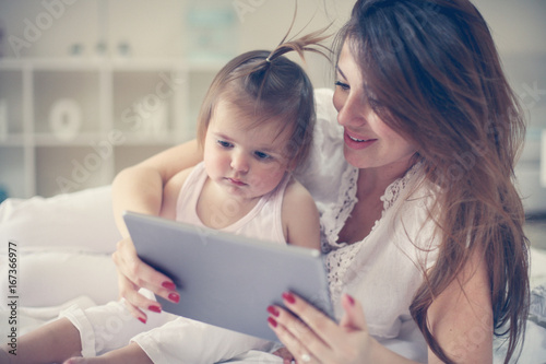 Mother and her little baby at home. Mother with her baby watching something on digital tablet.