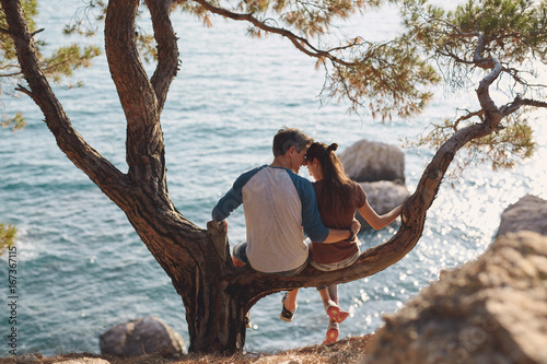 romantic young couple in love together. Happy young couple in love sitting and kissing on a tree branch on sea in background photo