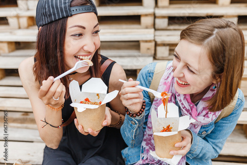 Fényképezés two girls friends enjoying a chinese take away wok noodle food in the street
