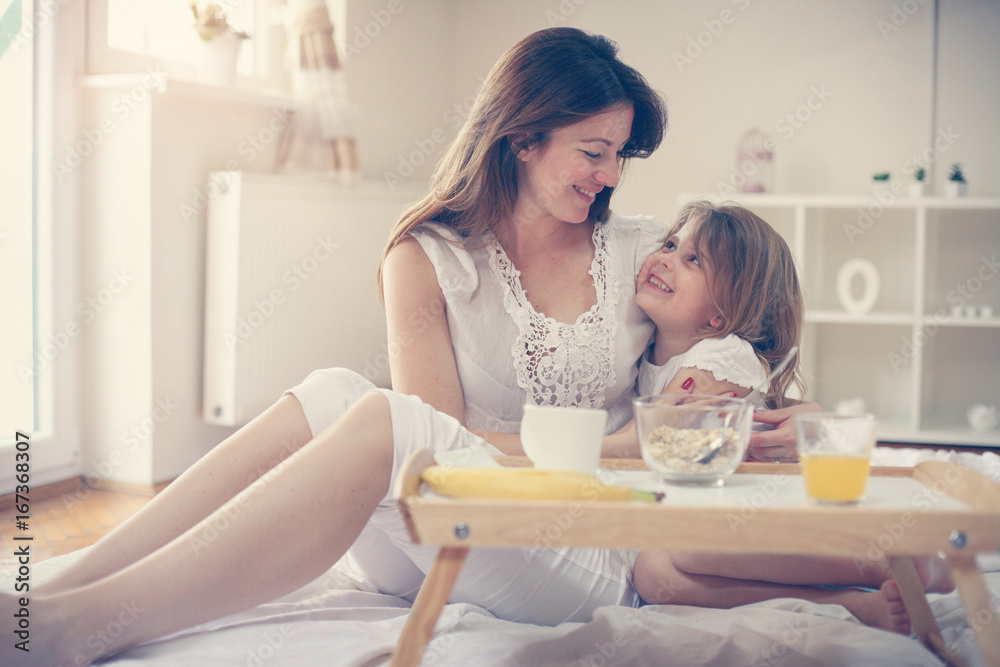 Mother with her little daughter having breakfast in the bed. Mother and her daughter enjoying a healthy breakfast together.