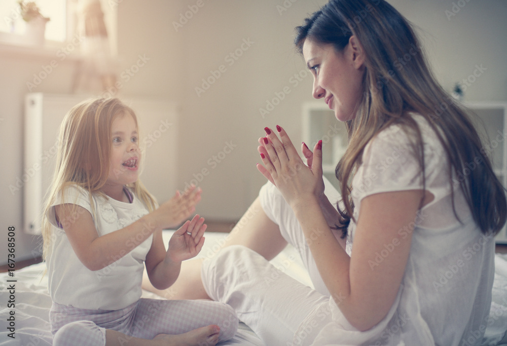 Mother with her cute little daughter sitting  on bed.