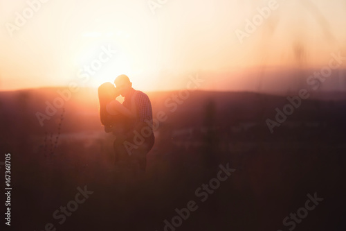 Lovers in mountains against background of fog and hills, a crimson, scarlet, red, orange sunset, sun shines in back, backlight, glare of sun. concept of first love and kiss of tender romantic