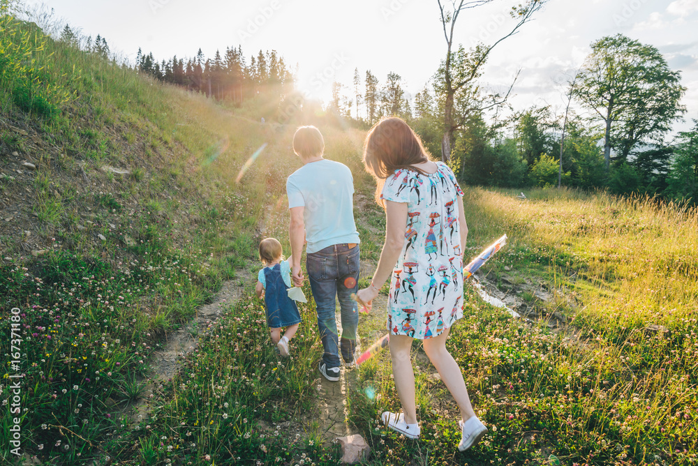 Fototapeta premium mother and father holding daughter hands and walking by mountains