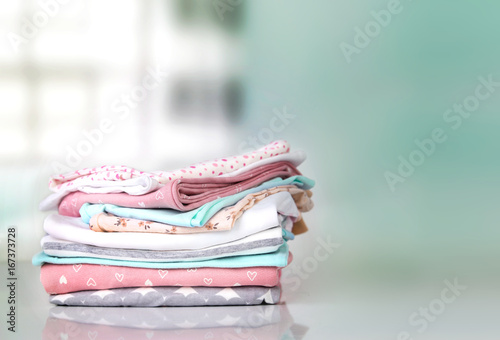 Pastel baby clothes stack pile empty space background.