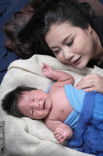 family portrait of young asian mum with her boy newborn in black background .