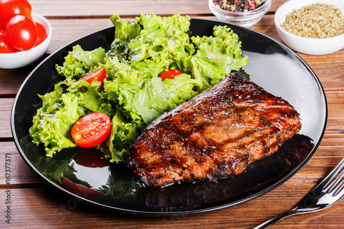 Grilled steak meat with fresh vegetable salad and tomatoes on black plate, wooden background