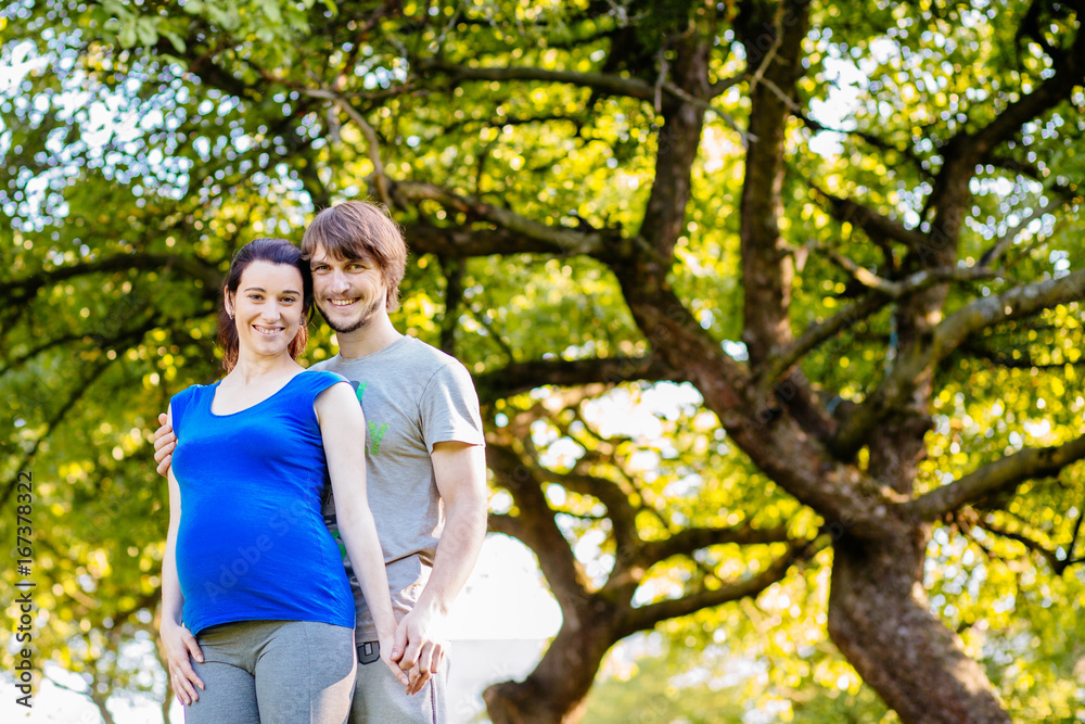 Pregnant couple over beautiful green tree background. Parenthood, sport and healthy life concept. Pregnant couple over beautiful green tree background. Parenthood, sport and healthy life concept.