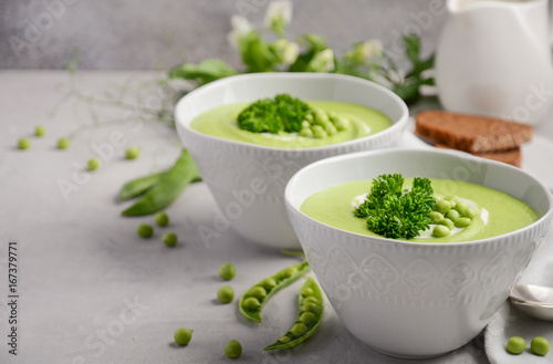 Green pea soup in bowls on grey concrete or stone background, selective focus, copy space